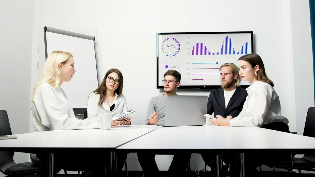 Réunion d'équipe discutant des usages de l’IA en entreprise avec des graphiques sur un écran.